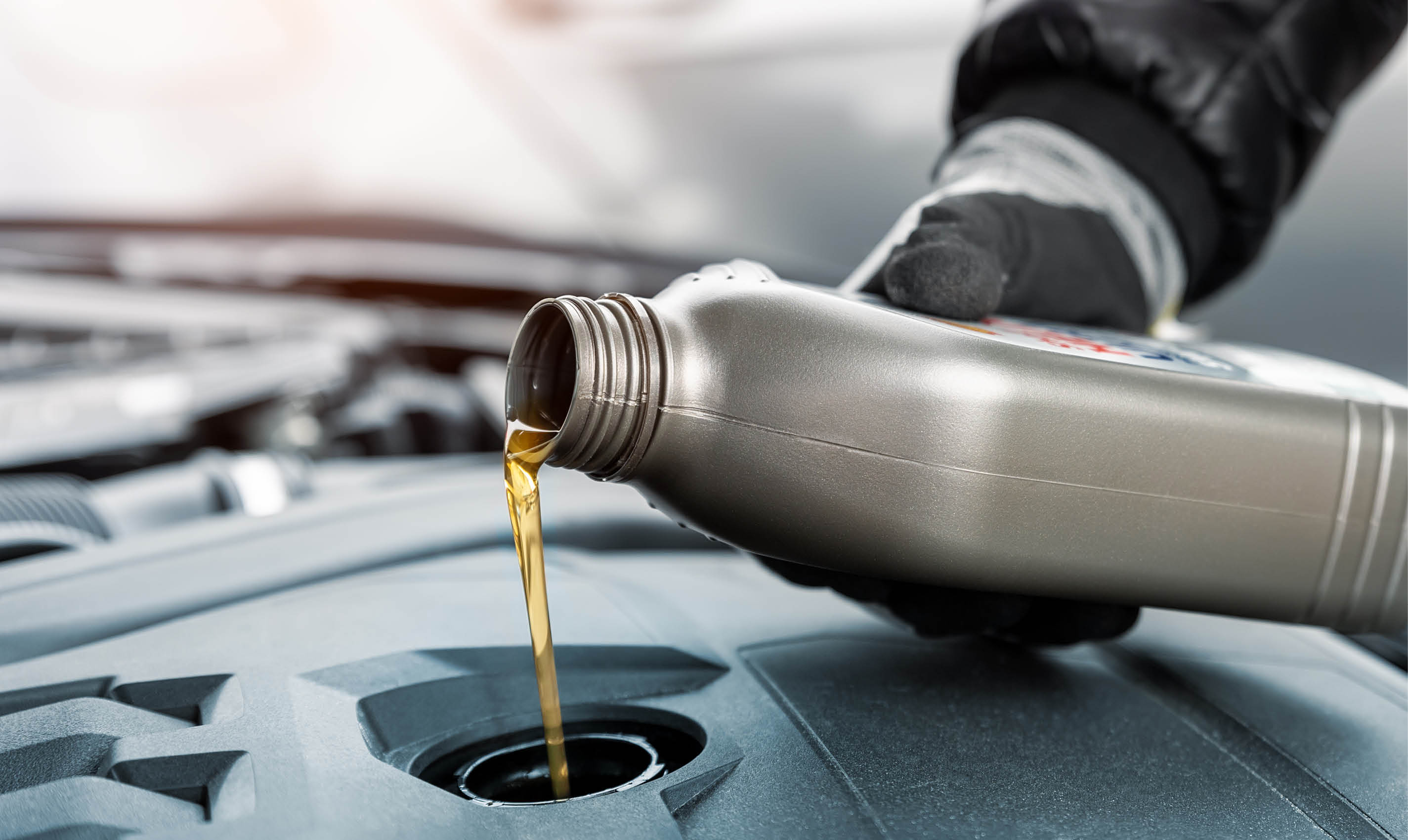Close-up driver hand holding small bottle can pouring synthetic motor oil in diesel or petrol turbocharged vehicle engine due oil consumption. New lubricant diy change. Car service maintenance work.